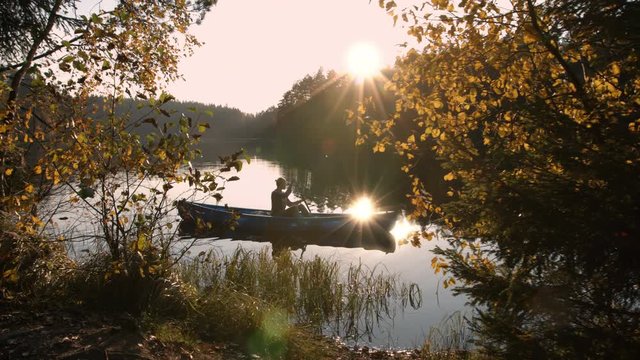 Woman with canoe paddling on calm lake at sunset