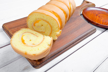 Roll cake  butter cream filling and on wooden plate over white wooden background