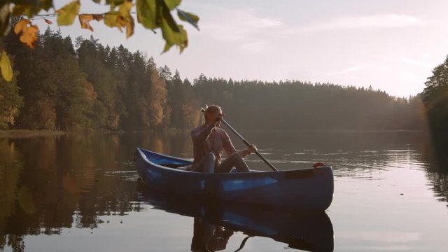 Woman with canoe paddling on calm lake at sunset