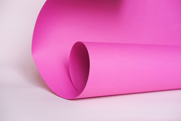 A sheet of pink paper rolled into a tube on a light background.