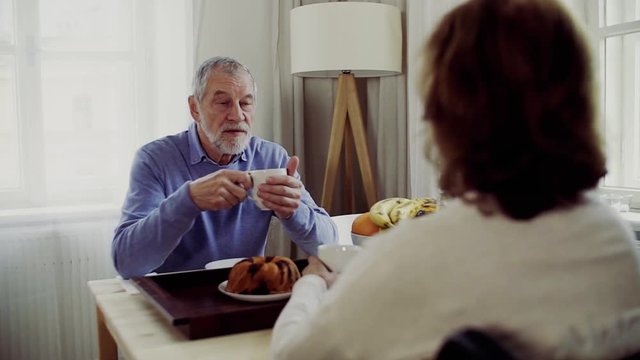 Senior couple with wheelchair sitting at the table at home, having breakfast and talking.