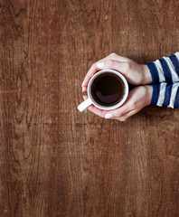 women's hands holding a cup of coffee on a wooden background