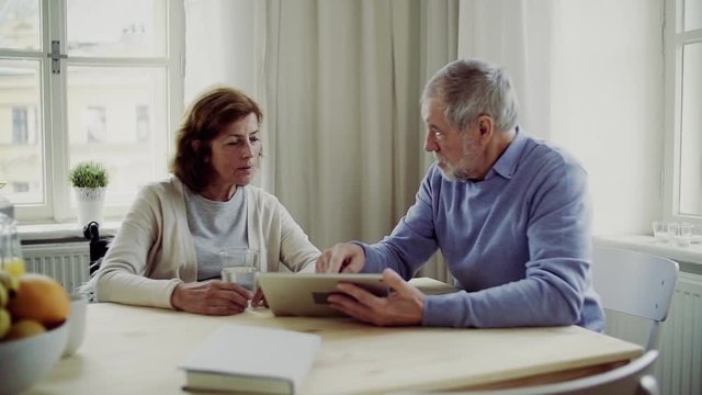 Senior couple with wheelchair and tablet sitting at the table at home, talking.
