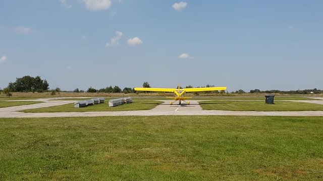 yellow plane with a propeller is on the track at the airport, propeller is working, rear view