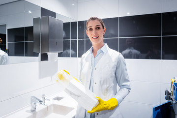 Janitor woman changing paper towels in public restroom