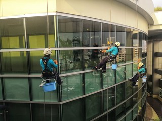 Rope access cleaning worker wearing safety harness hard hat working at height descending on rope...