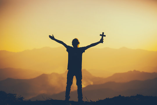 Man standing holding christian cross for worshipping God at sunset background. christian silhouette concept.