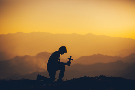 Young man sitting down and praying to God at sunset background. christian silhouette concept.