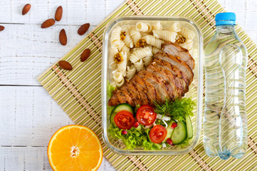 Lunch box: rotini with baked chicken breast and salad on a white wooden background. Top view, flat lay. Delicious healthy lunch. The concept of healthy eating.