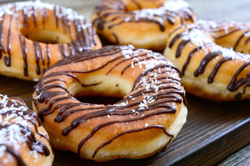Homemade classic donuts with chocolate and coconut flakes on a dark wooden background. Close up.