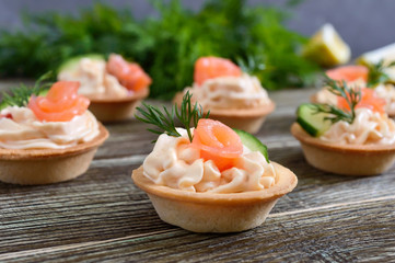 Tartlets with cream cheese and salted salmon on a wooden background. Tasty light snack for a party. Finger Food.