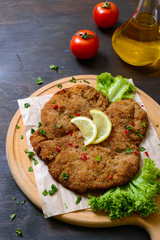 Large Viennese schnitzel on a wooden board with lemon on a dark background. Meat dish