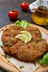 Large Viennese schnitzel on a wooden board with lemon on a dark background. Meat dish