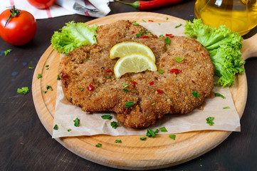 Large Viennese schnitzel on a wooden board with lemon on a dark background. Meat dish