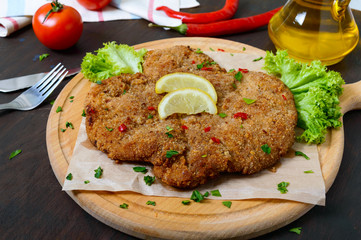 Large Viennese schnitzel on a wooden board with lemon on a dark background. Meat dish