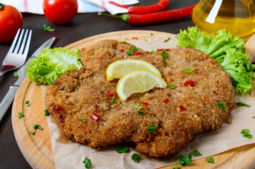 Large Viennese schnitzel on a wooden board with lemon on a dark background. Meat dish