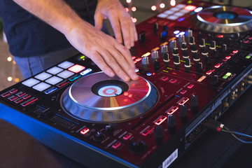DJ is mixing some music with controller at outdoor night party, by moving hand to scratching