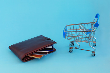 Shopping cart and credit cards in the wallet on blue background.