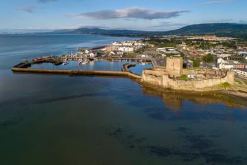 Medieval Norman Castle in Carrickfergus near Belfast in sunrise light. Aerial view with marina, yachts, parking, town and far view of Belfast in the background