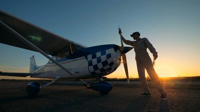 Male pilot wipes a plane's propeller, side view.