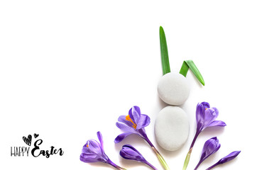 Bunny from sea stones on a white background among crocuses. Spring easter greeting card. Top view. Copy space. Mock-up