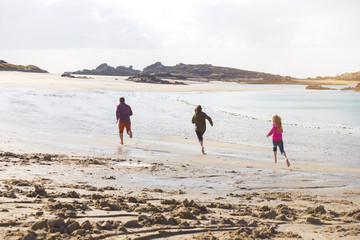 Dad and two daughters running along the beach
