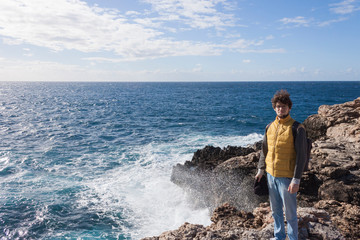man tourist in yellow vest with backpack on rock cliff in Malta