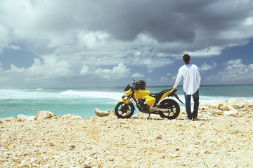 Young handsome man standing near motorcycle on the tropical beach. © Kitja