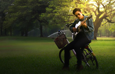Obraz na płótnie Canvas Young man holding a guitar.young men sitting on a bicycle seat and playing guitar in the park.freedom lifestyle.