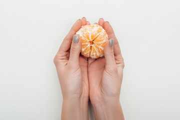 partial view of woman holding peeled whole tangerine on white background