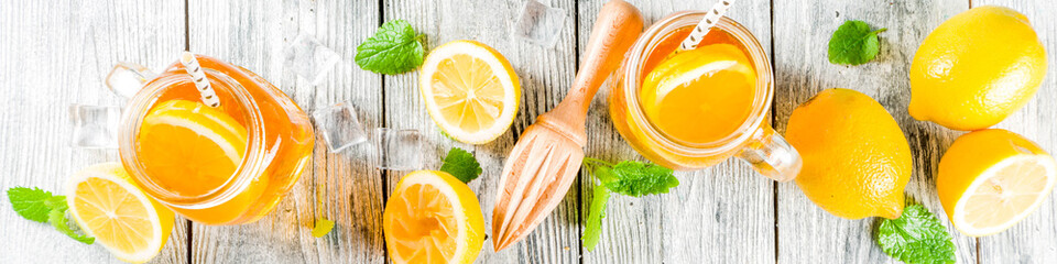 Iced summer drink, tea with lemon slices and mint, rustic wooden background copy space banner