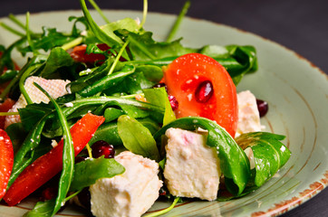 Fresh spring salad with rucola, feta cheese, red onion and pomegranate seeds in black bowl on chalkboard background.