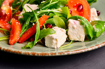 Fresh spring salad with rucola, feta cheese, red onion and pomegranate seeds in black bowl on chalkboard background.