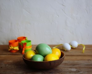 Colorful easter eggs in a brown bowl. Wooden table, light background. Copy space, horizontal orientation