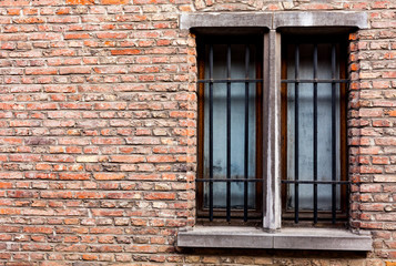 Fototapeta na wymiar Old house with copy space on the red bricks wall. Old wooden windows with metal bars on the old brick house