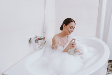 Happy young woman applying shower gel in the bathroom