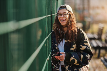 Beautiful mixed race teenage girl laughing and listening music while leaning on the fence.