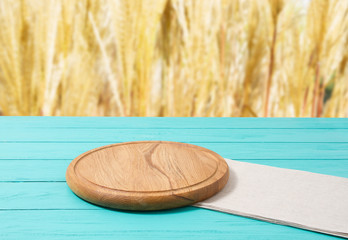 Cutting board for pizza and napkin tablecloth on blue wooden kitchen table. Blur rye yellow bokeh background. Copy space. Selective focus.