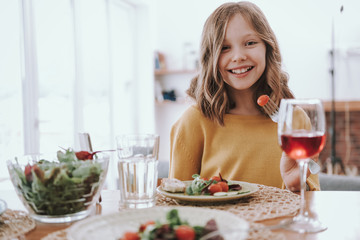 Joyful little girl in yellow sweater having dinner at home