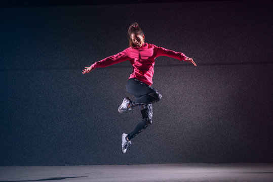 Vital sporty young girl jumping against black wall.