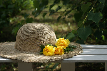 straw hat and three yellow roses on a green blurred background