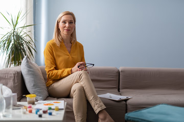 Smiling female psychologist holding eyeglasses in arms during art therapy seance