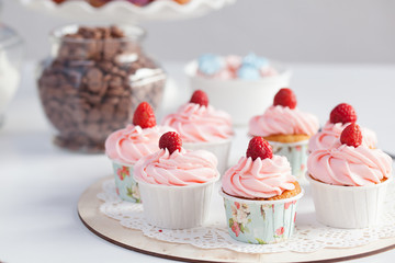 cupcakes with pink cream and raspberries on a wooden plate