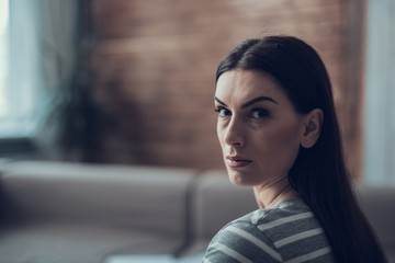 Brunette depressed lady looking at camera in apartment indoors