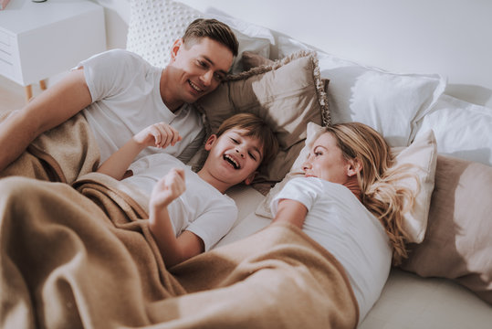 Positive boy lying in bed with parents and laughing