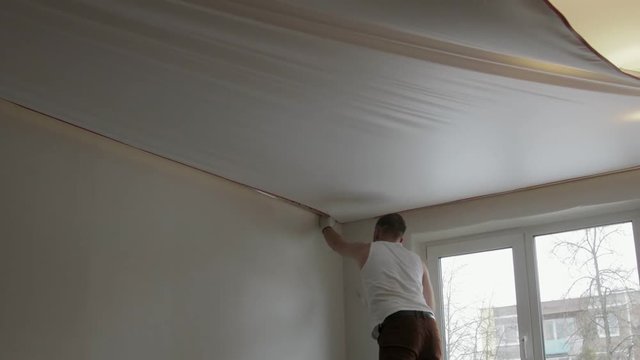 Static General plan of a young man installing a canvas of white stretch ceiling in the room of the apartment