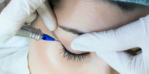 Permanent make-up tattoo. Cosmetologist applying permanent make up eyeliner, eyeliner tattoo procedure on young woman in beauty salon, extreme close up