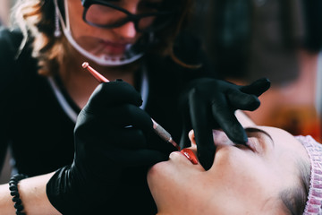 Permanent make-up for red Lips of beautiful woman in beauty salon. Closeup beautician doing tattooing Lips.