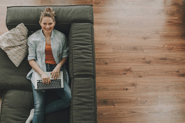 Cheerful female laying on couch with laptop