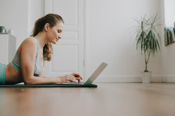 Smiling woman laying on yoga mat with laptop